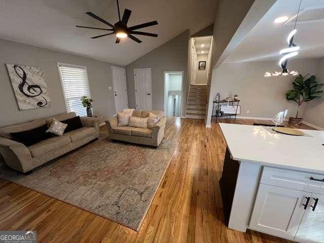 living room featuring ceiling fan with notable chandelier, light hardwood / wood-style flooring, and lofted ceiling