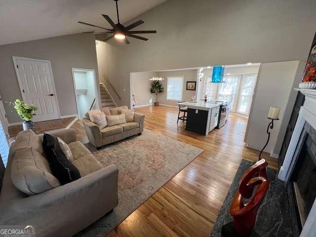 living room featuring light hardwood / wood-style flooring, high vaulted ceiling, and ceiling fan with notable chandelier