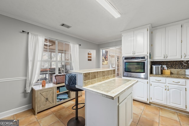 kitchen with a breakfast bar area, a center island, white cabinets, decorative backsplash, and oven