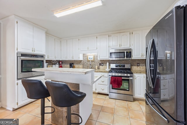 kitchen with light tile patterned floors, white cabinetry, a kitchen bar, stainless steel appliances, and a kitchen island