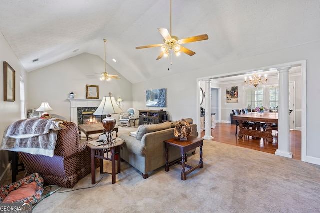 carpeted living room featuring decorative columns, vaulted ceiling, ceiling fan with notable chandelier, and a high end fireplace