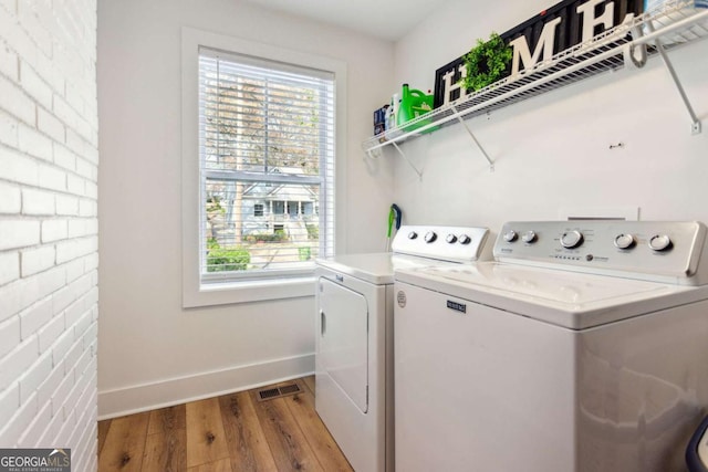 clothes washing area featuring light wood-type flooring, washing machine and dryer, and plenty of natural light