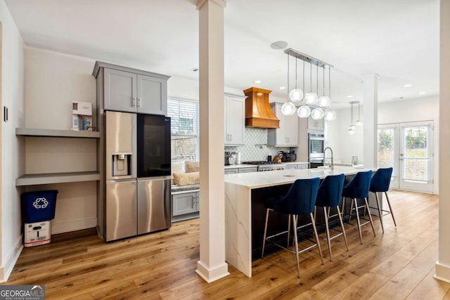 kitchen with gray cabinetry, a breakfast bar area, decorative backsplash, custom range hood, and appliances with stainless steel finishes