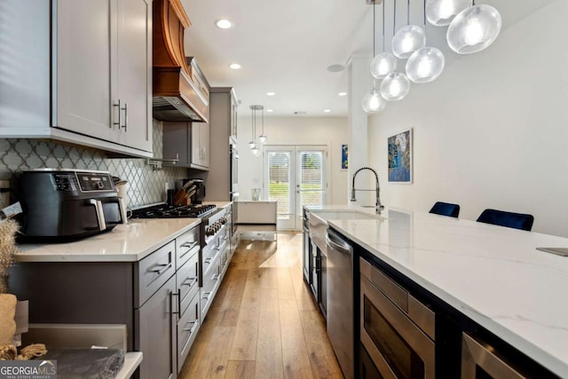 kitchen with light wood-type flooring, light stone counters, stainless steel appliances, sink, and pendant lighting