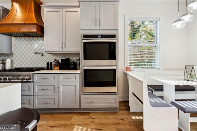 kitchen featuring hanging light fixtures, gray cabinets, light wood-type flooring, custom range hood, and stainless steel appliances