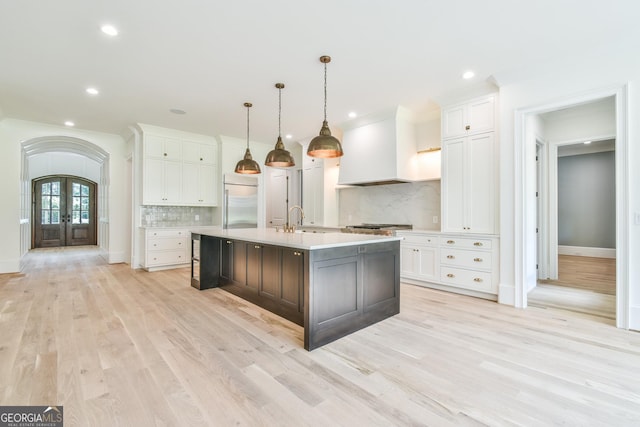 kitchen with stainless steel built in fridge, white cabinets, backsplash, and an island with sink