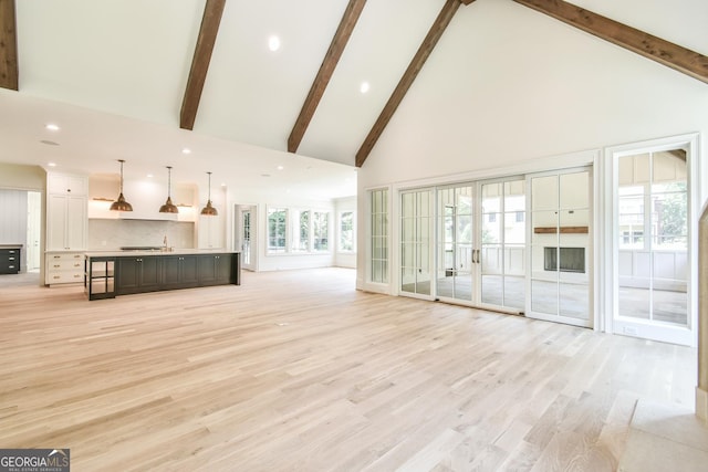 unfurnished living room with high vaulted ceiling, french doors, and light wood-type flooring