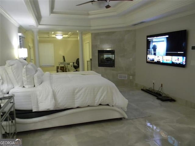 bedroom featuring ceiling fan, ornamental molding, a tiled fireplace, a raised ceiling, and ornate columns