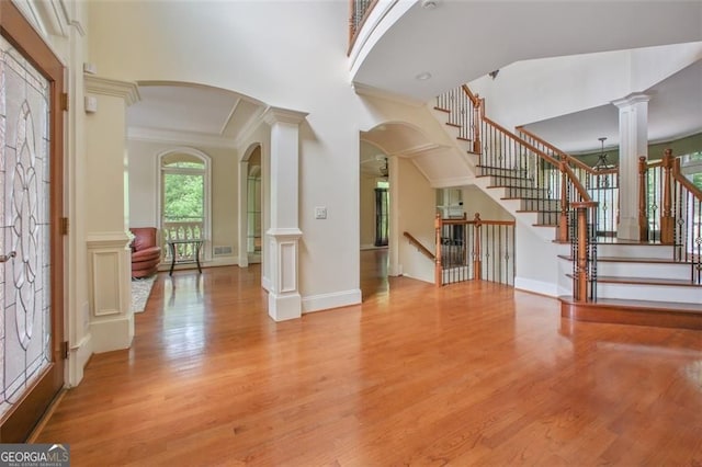 entrance foyer featuring crown molding, light hardwood / wood-style floors, decorative columns, and a high ceiling