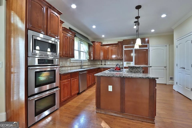 kitchen featuring built in appliances, hanging light fixtures, a center island, and dark stone counters