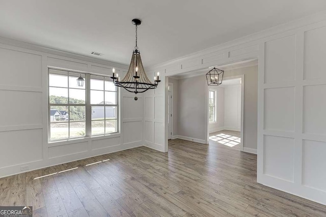 unfurnished dining area featuring a chandelier, hardwood / wood-style floors, and crown molding