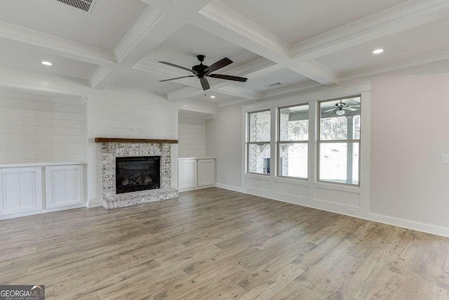 unfurnished living room with beam ceiling, a stone fireplace, light wood-type flooring, and coffered ceiling