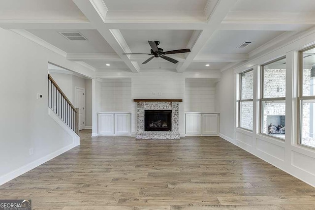 unfurnished living room with coffered ceiling, ceiling fan, beamed ceiling, a fireplace, and light hardwood / wood-style floors