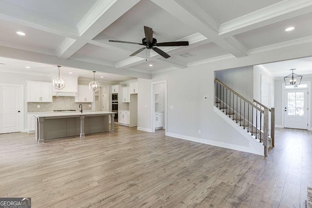 unfurnished living room featuring beamed ceiling, ceiling fan with notable chandelier, light hardwood / wood-style floors, and coffered ceiling