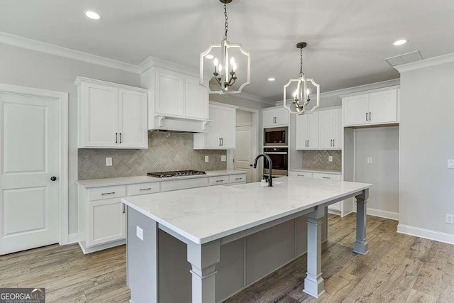 kitchen with white cabinets, appliances with stainless steel finishes, light stone countertops, and a kitchen island with sink