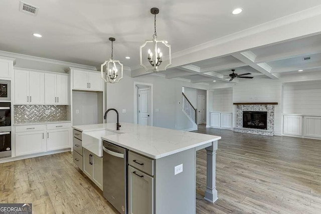 kitchen featuring coffered ceiling, stainless steel appliances, a kitchen island with sink, sink, and beamed ceiling