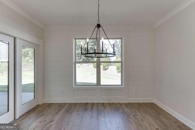 unfurnished dining area with hardwood / wood-style flooring, crown molding, and a notable chandelier