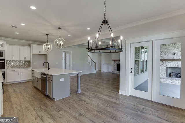 kitchen with hanging light fixtures, a brick fireplace, tasteful backsplash, a center island with sink, and white cabinets