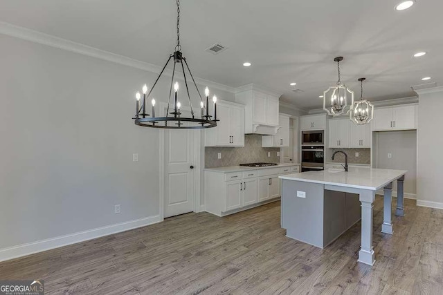 kitchen featuring ornamental molding, pendant lighting, stainless steel appliances, and a center island with sink