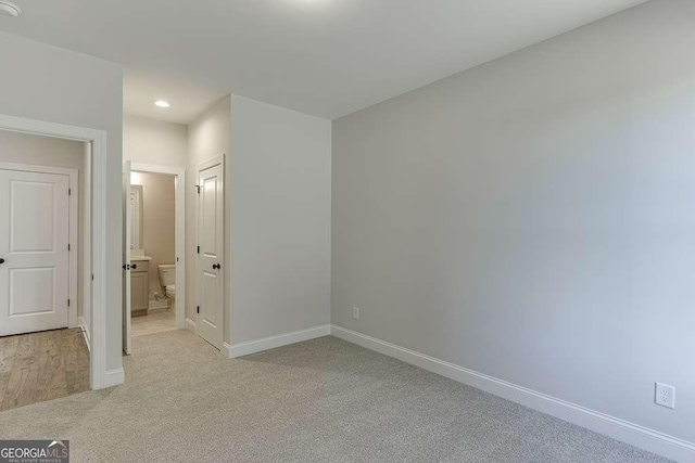 unfurnished bedroom with light colored carpet and connected bathroom