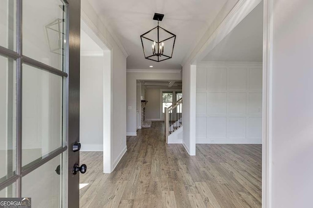 foyer featuring light wood-type flooring, ornamental molding, and a notable chandelier