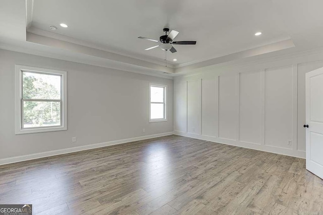 empty room featuring a raised ceiling, ceiling fan, and light hardwood / wood-style flooring