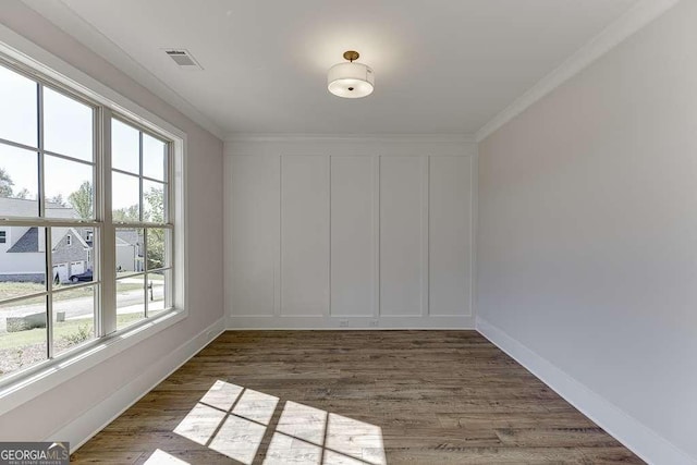 empty room with a healthy amount of sunlight, dark hardwood / wood-style flooring, and ornamental molding