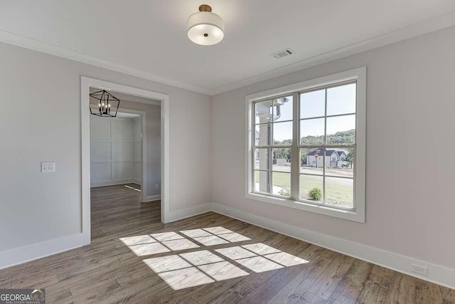 spare room featuring crown molding, hardwood / wood-style floors, and a notable chandelier