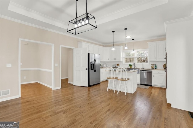 kitchen with hanging light fixtures, a kitchen island, a kitchen bar, white cabinetry, and stainless steel appliances