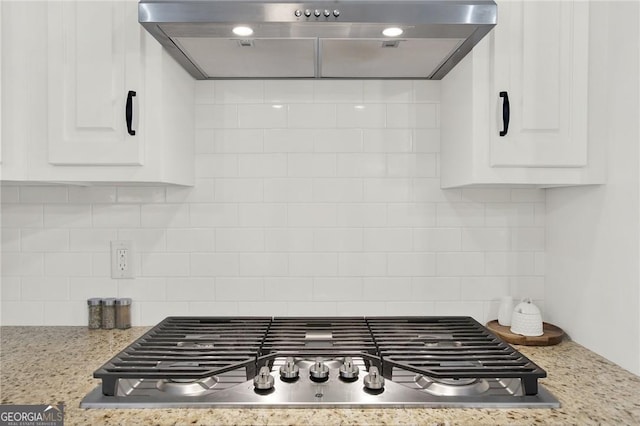 room details featuring white cabinetry, stainless steel gas cooktop, light stone counters, range hood, and backsplash