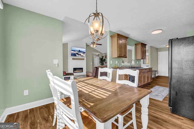 dining area featuring a large fireplace, ceiling fan, dark wood-type flooring, sink, and lofted ceiling