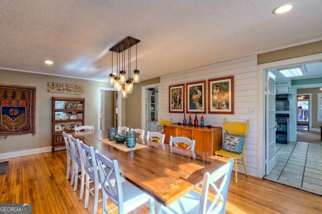 dining area featuring a textured ceiling, an inviting chandelier, light hardwood / wood-style flooring, and wooden walls