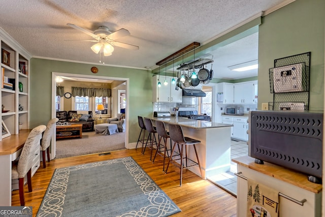 kitchen with range, white cabinets, light hardwood / wood-style floors, kitchen peninsula, and a breakfast bar area