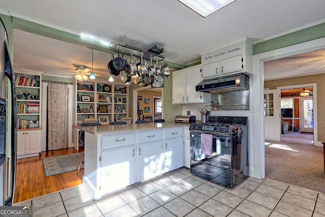 kitchen with kitchen peninsula, light stone countertops, light carpet, black gas range oven, and white cabinets