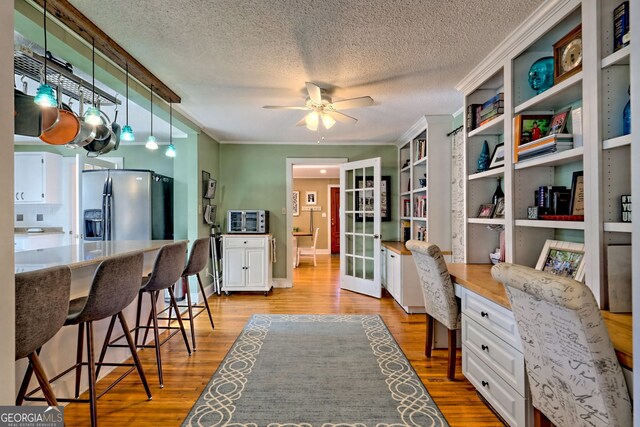 interior space featuring ceiling fan, ornamental molding, a textured ceiling, and light hardwood / wood-style flooring