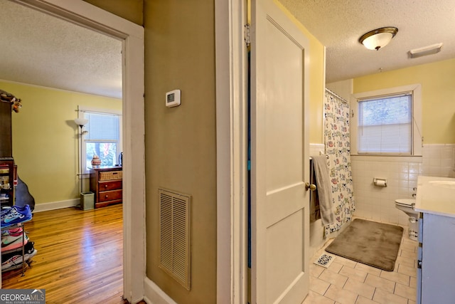 full bathroom with vanity, toilet, shower / bathtub combination with curtain, a textured ceiling, and tile walls