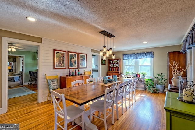 dining space with wood walls, light hardwood / wood-style flooring, a textured ceiling, and an inviting chandelier