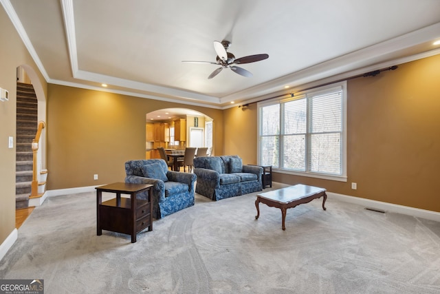 living room featuring a tray ceiling, crown molding, ceiling fan, and light colored carpet