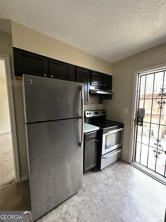 kitchen with appliances with stainless steel finishes, dark cabinets, light countertops, under cabinet range hood, and tile walls