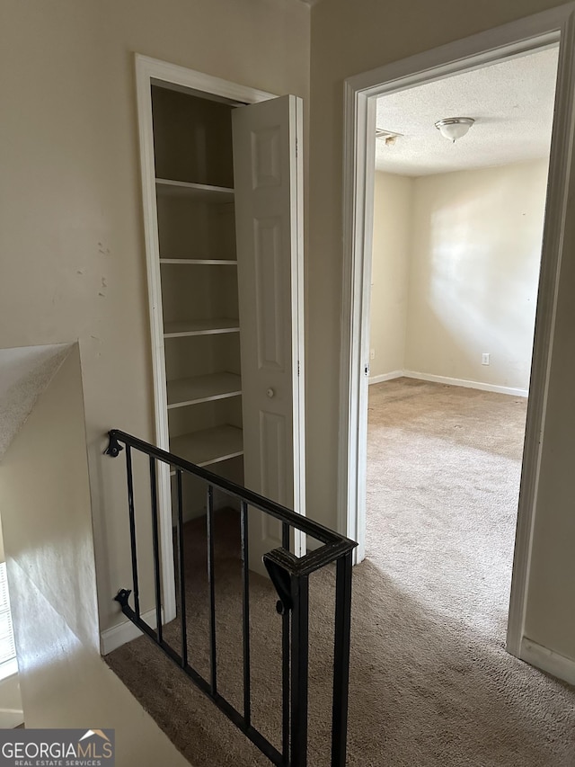 hall featuring carpet floors, a textured ceiling, baseboards, and stairs