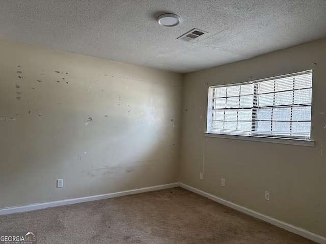 empty room featuring carpet floors, baseboards, visible vents, and a textured ceiling