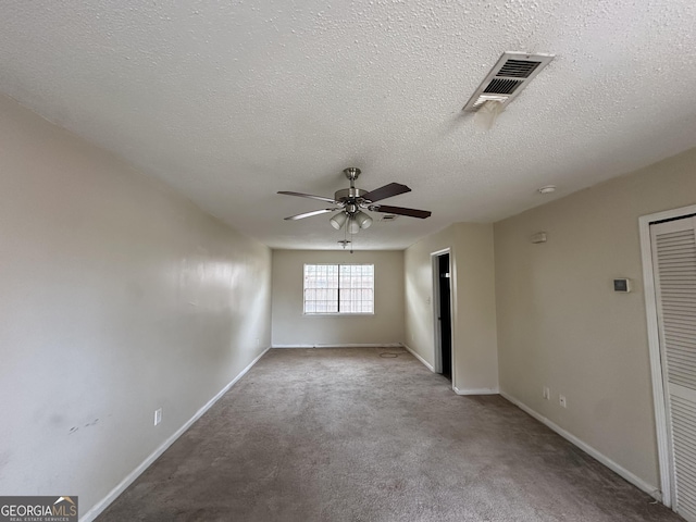 empty room featuring a textured ceiling, light colored carpet, a ceiling fan, baseboards, and visible vents