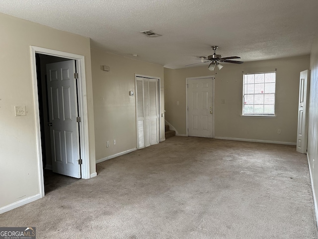 interior space with a closet, light colored carpet, visible vents, a textured ceiling, and baseboards