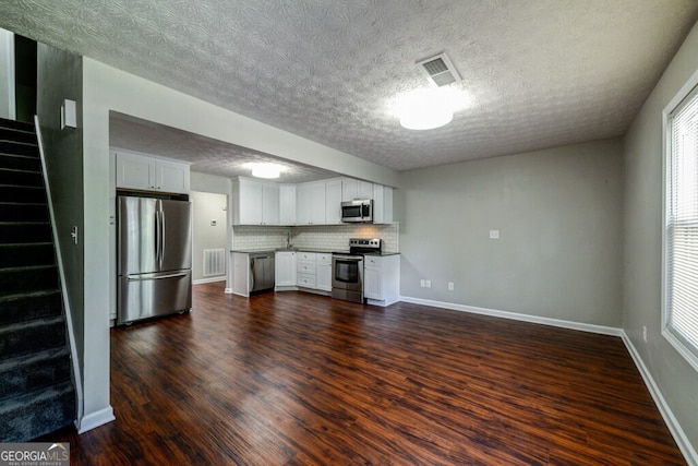 kitchen featuring dark wood-type flooring, backsplash, a textured ceiling, white cabinets, and appliances with stainless steel finishes