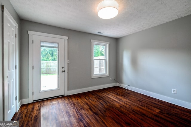 doorway to outside featuring a textured ceiling, a healthy amount of sunlight, and dark wood-type flooring