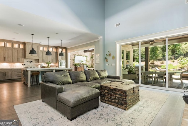 living room with a towering ceiling, crown molding, ceiling fan, and dark wood-type flooring