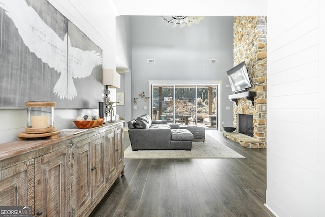 living room with a stone fireplace, dark wood-type flooring, a high ceiling, and a notable chandelier