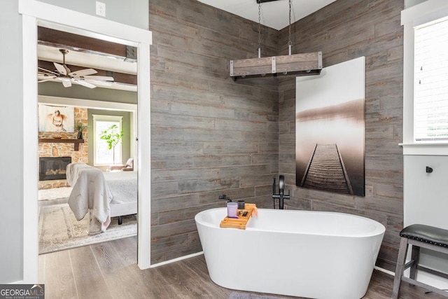 bathroom featuring ceiling fan, a fireplace, a tub to relax in, beam ceiling, and wood-type flooring