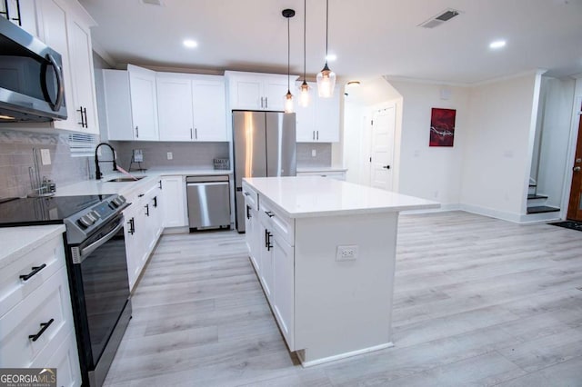 kitchen with white cabinets, light hardwood / wood-style flooring, appliances with stainless steel finishes, decorative light fixtures, and a kitchen island