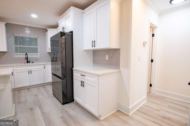 kitchen with backsplash, black fridge, sink, and white cabinetry